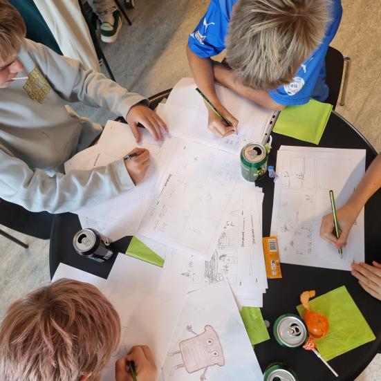 En gruppe drenge sidder og tegner på biblioteket.