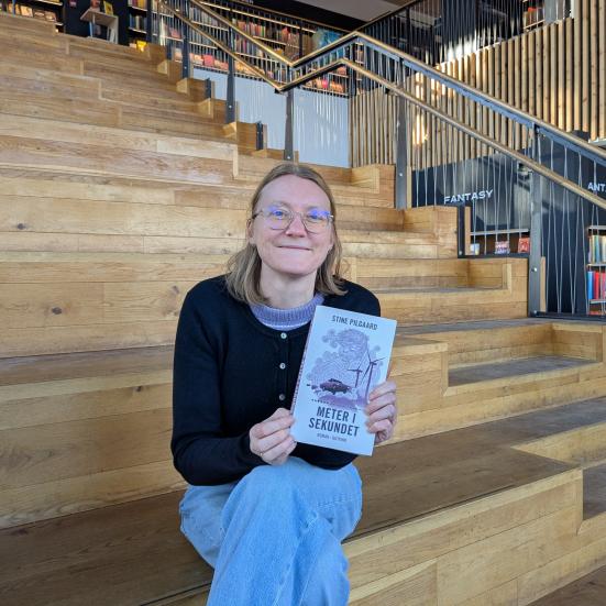 Lea sidder på trappen på biblioteket i Gilleleje med et eksemplar af bogen.