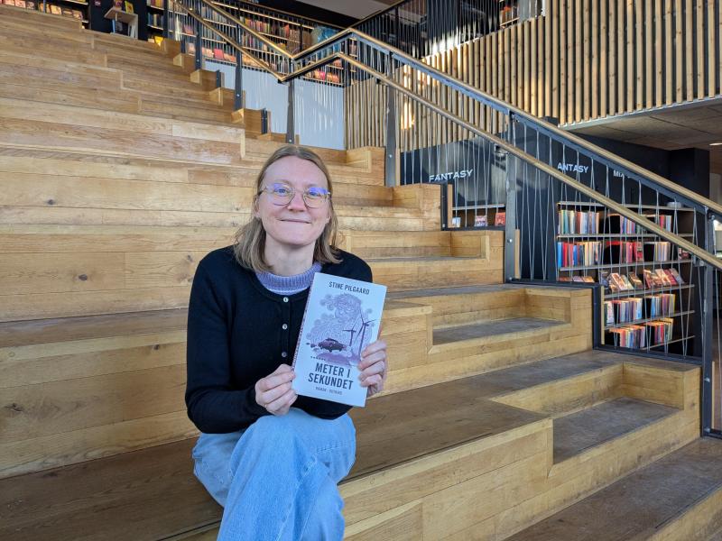 Lea sidder på trappen på biblioteket i Gilleleje med et eksemplar af bogen.