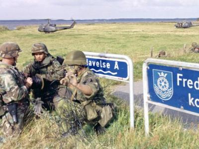 Tre soldater med to militærhelikoptere i baggrunden.