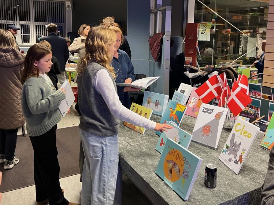 To af de unge står foran et bord med dug, hvor deres bøger er udstillet.