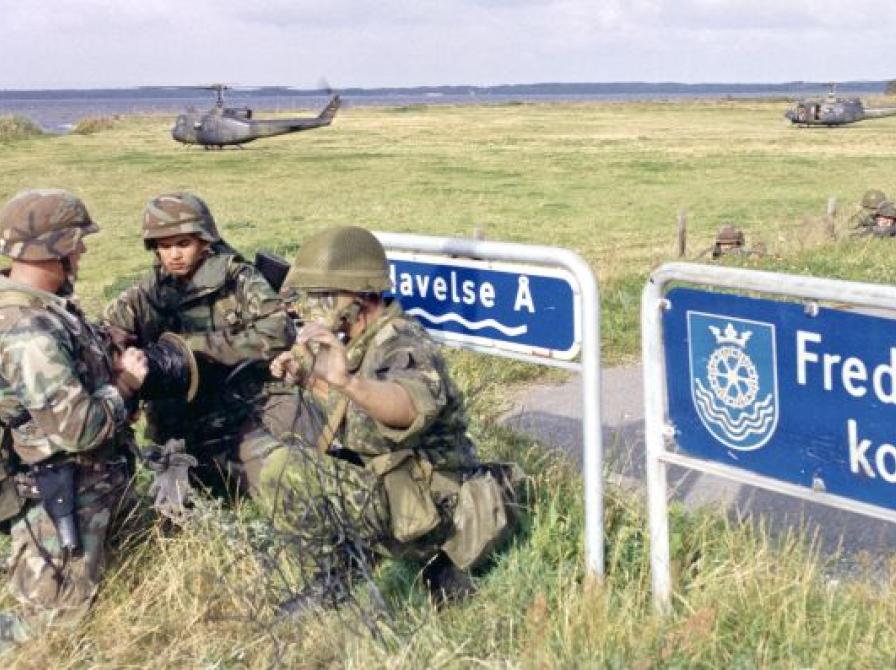 Tre soldater med to militærhelikoptere i baggrunden.