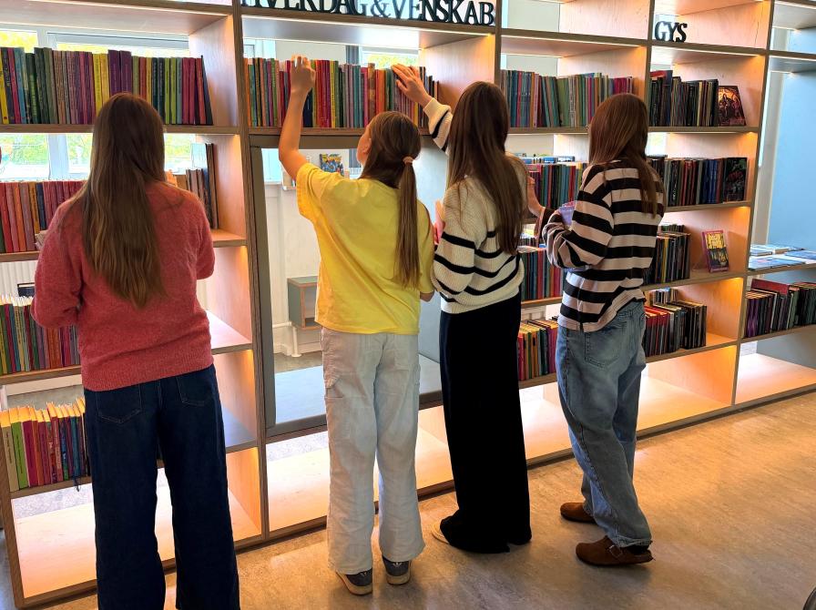 Fire piger står og kigger på bøger foran en bogreol på børnebiblioteket i Helsinge.